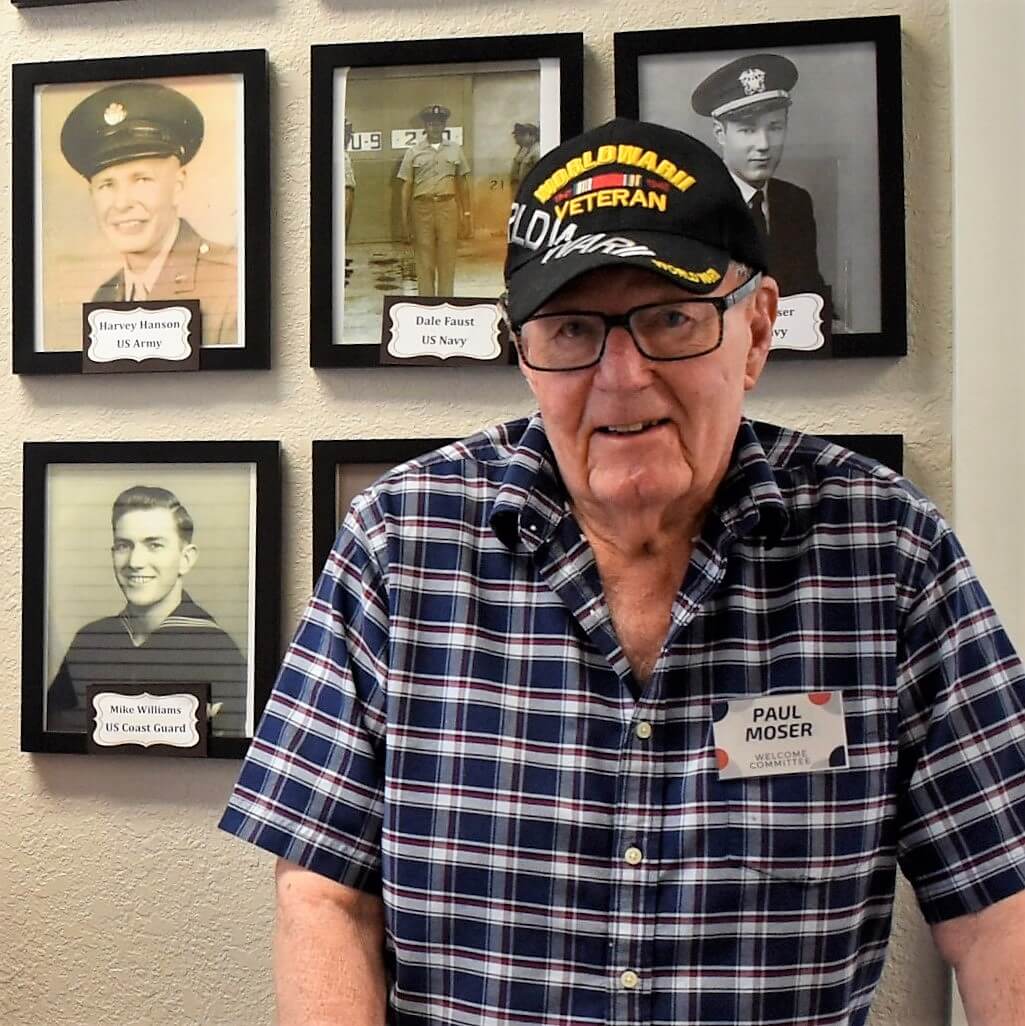 Carlton Senior Living resident, Paul Moser, poses in front of the veteran wall in Pleasant Hill.