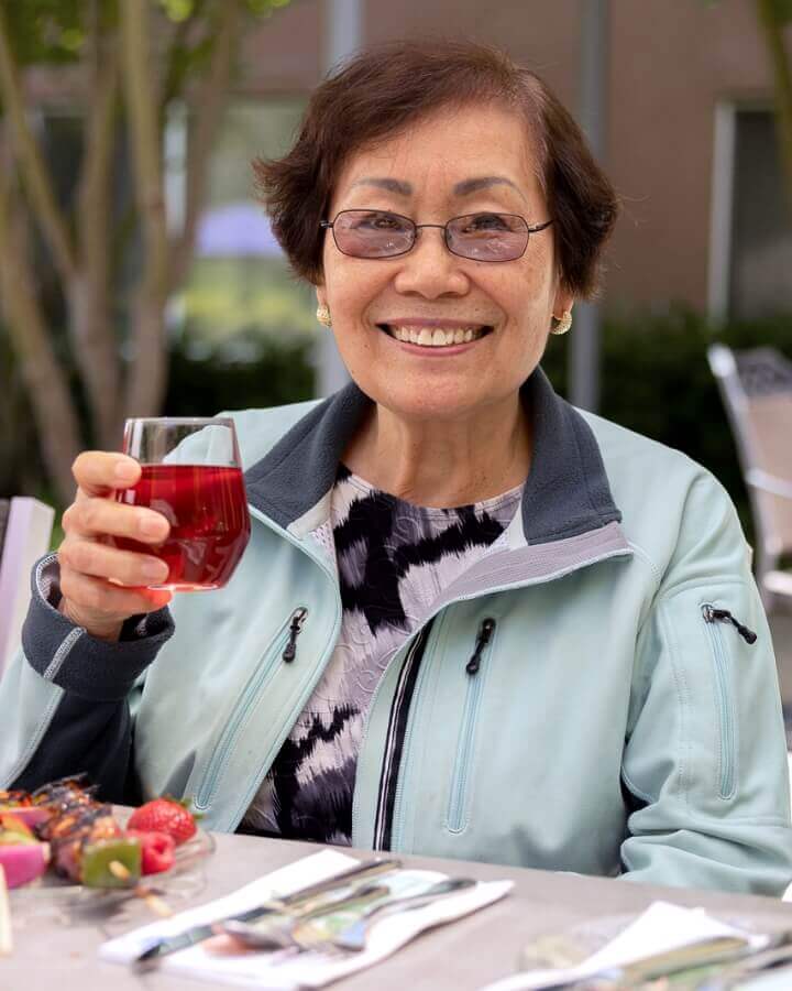 An elderly woman with glasses enjoys a beverage and outdoor social time at Carlton Senior Living.