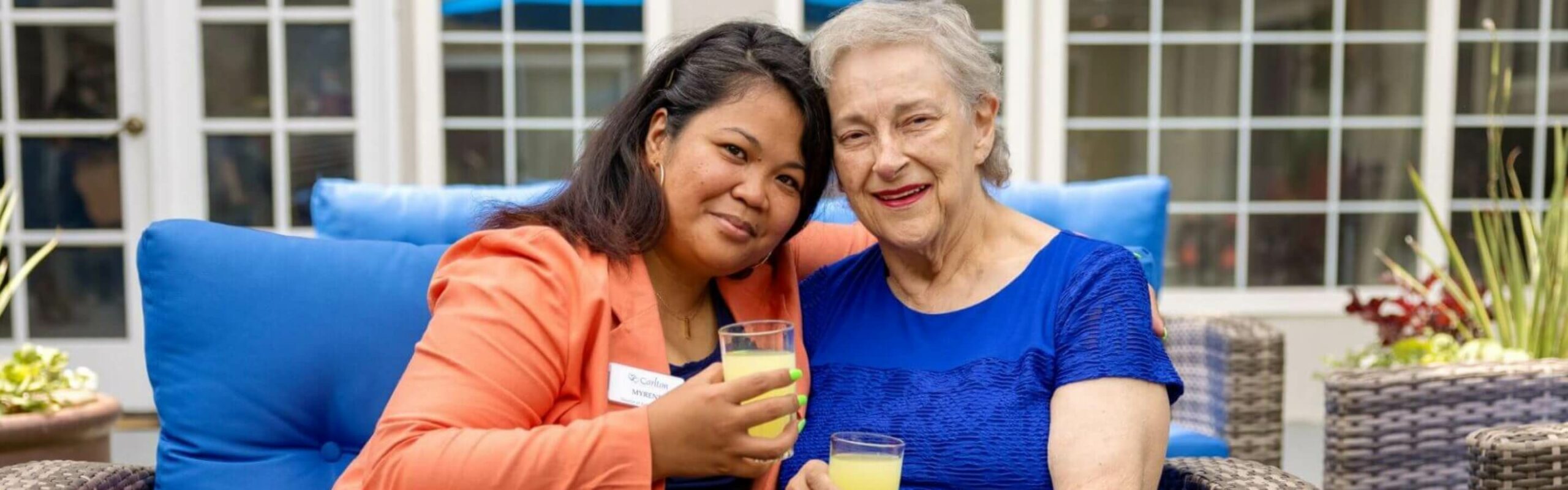 An elderly woman shares a moment with a Carlton team member, both holding beverages, showcasing the close-knit community at Carlton Senior Living.