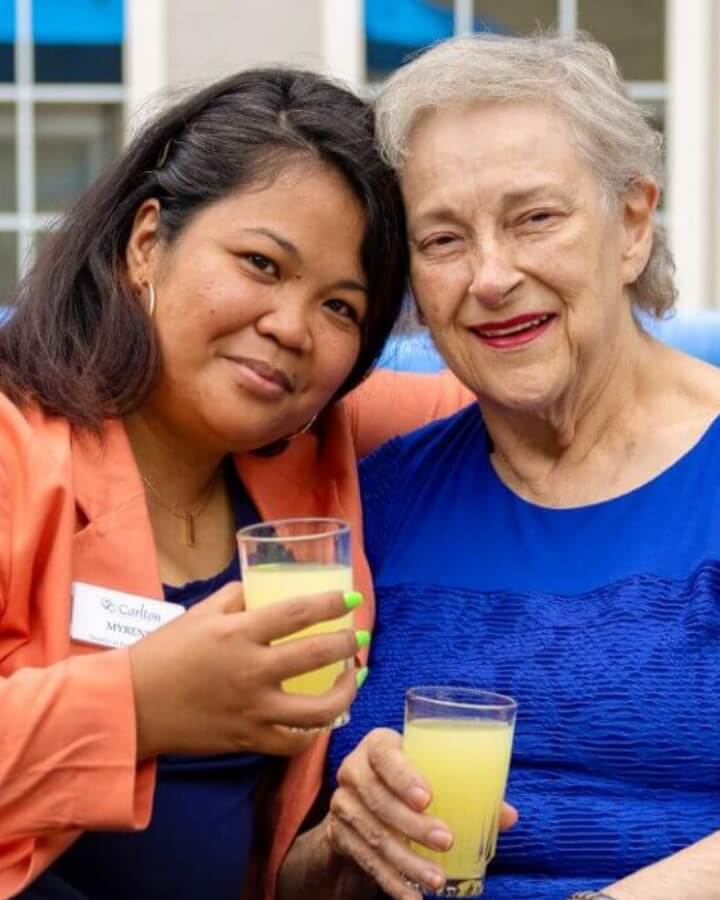 An elderly woman shares a moment with a Carlton team member, both holding beverages, showcasing the close-knit community at Carlton Senior Living.